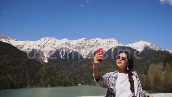 年轻漂亮的女人在山上用智能手机自拍视频的预览图