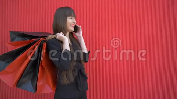 购物日兴高采烈的女孩在手机上谈论她手里拿着纸袋的成功购物视频的预览图