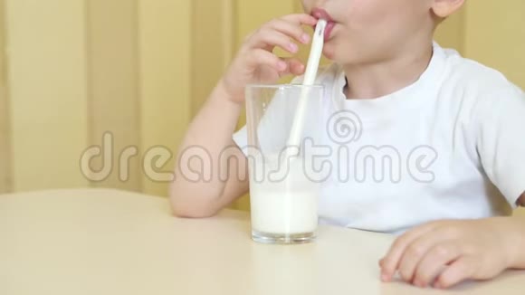 一个快乐的孩子坐在桌子旁通过吸管从杯子里喝牛奶把摄像机从下往上移视频的预览图