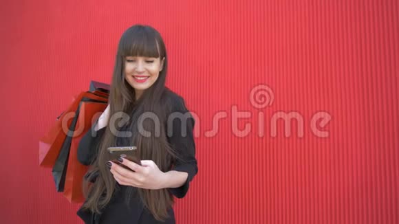 购物时间快乐的女士使用智能手机带着红色背景的纸袋微笑视频的预览图