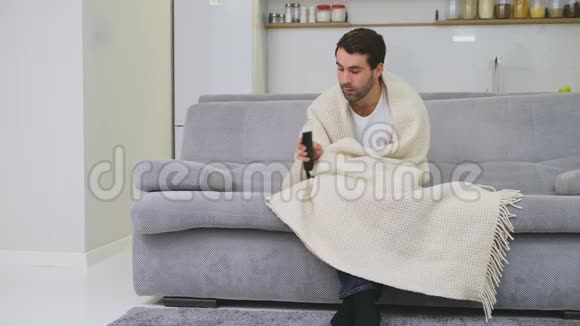 一个穿着毯子坐在沙发上的人是尽可能冷的家里的人病人灰色沙发里视频的预览图