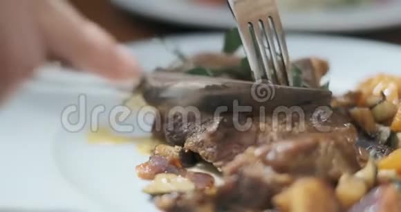 男人的手是用刀子切肉牛排的特写有人在餐馆里吃油腻的食物视频的预览图