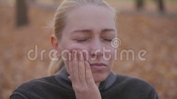 牙痛一个牙齿疼痛的女人坐在长凳上的公园里视频的预览图