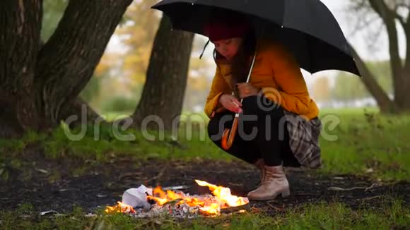 一个女人坐在火堆里在雨下撑着大伞视频的预览图
