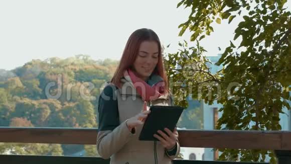 有狐毛的女孩站在户外在阳光明媚的天气里使用平板电脑并在网上订购视频的预览图