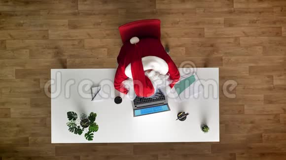 疲惫的圣诞老人坐着笔记本电脑在办公室里睡觉鸟瞰自上而下的拍摄视频的预览图