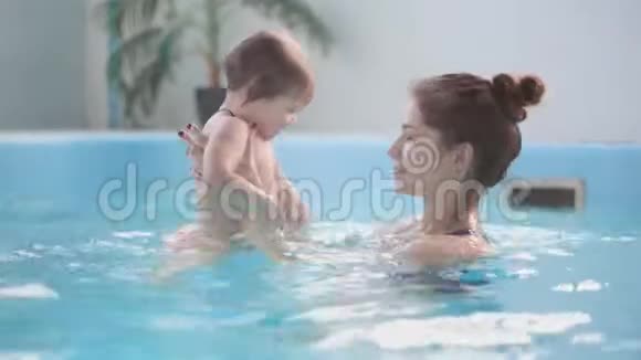 戴着防护眼镜的可爱金发幼儿正和他的母亲一起在游泳池里潜水视频的预览图