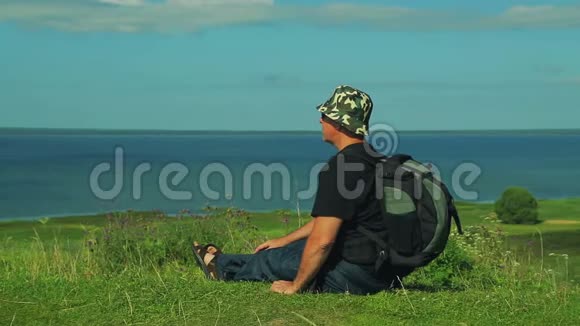 一个背着背包的人坐在山的边缘欣赏着湖的景色射击视频的预览图
