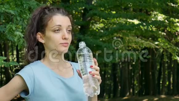 健身布鲁内特女士在绿色树木背景下跑步后在公园里喝水视频的预览图