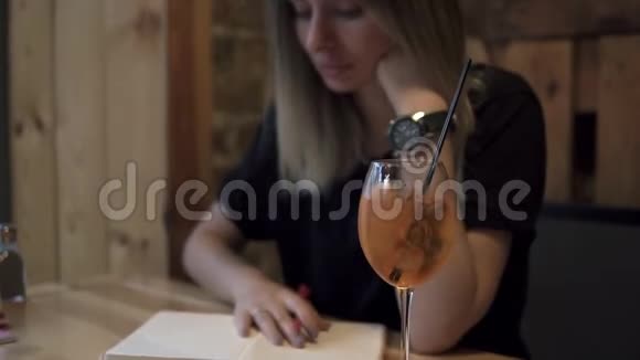 长发金发的女人坐在一家现代化的咖啡馆里在她的笔记本上做了一些笔记一杯酒视频的预览图