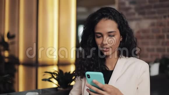 漂亮的女人使用智能手机坐在咖啡馆或同事办公室喝茶成功的肖像视频的预览图