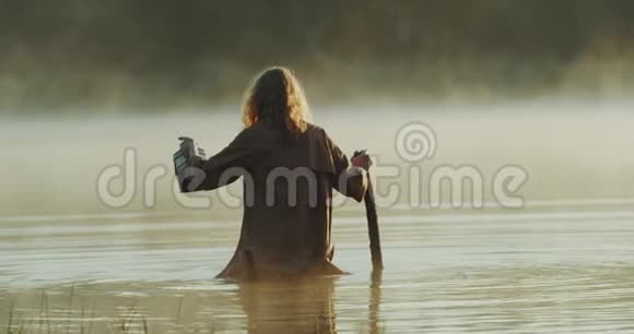 美丽的女孩走过一个神秘的湖与一根棍子和一个盒子然后她失去了她的棍子在湖里视频的预览图