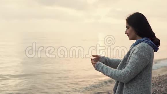 女人正试图用智能手机拍摄日落自拍站在海边视频的预览图