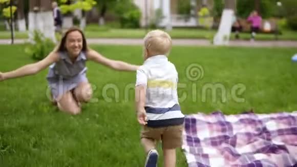 小金发男孩跑到他妈妈身边妈妈张开双手微笑着抓住了孩子快乐的母亲慈爱的儿子视频的预览图