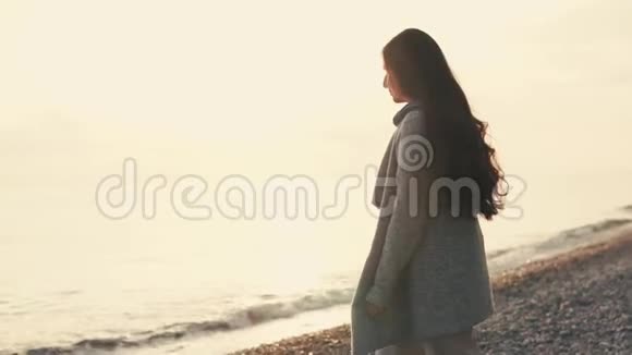 年轻苗条的黑发女人正在海滩上跳跃看着夕阳下的潮水视频的预览图