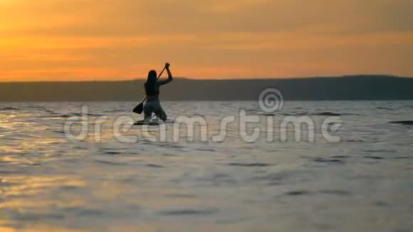 冲浪女孩漂浮在冲浪板上景色宜人女人在水中冲浪时拉桨视频的预览图