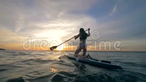 晚上女性冲浪者在开阔的海洋里骑桨板4K视频的预览图