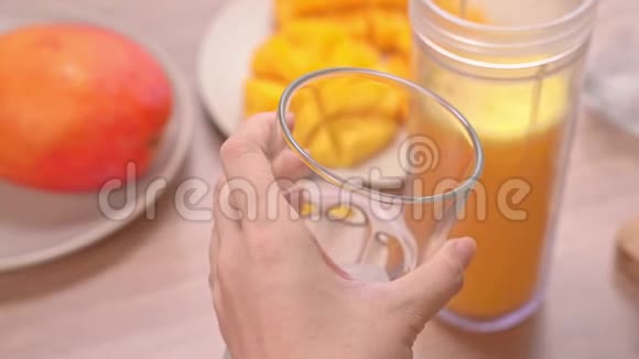 女人在明亮的木桌背景下在夏天的厨房里做新鲜的芒果汁健康自制概念视频的预览图