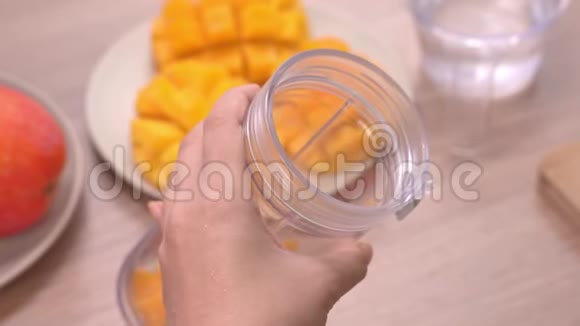 女人在明亮的木桌背景下在夏天的厨房里做新鲜的芒果汁健康自制概念视频的预览图