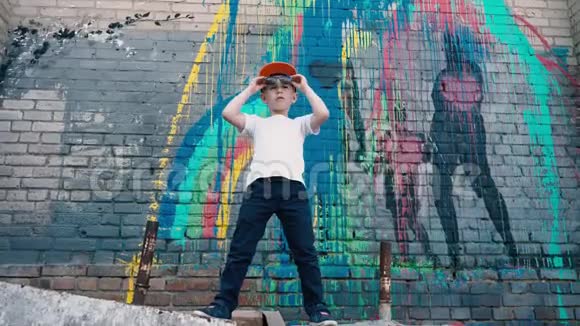 一个很酷的5岁孩子戴着墨镜在砖墙边跳着涂鸦一个年轻的街头舞者视频的预览图