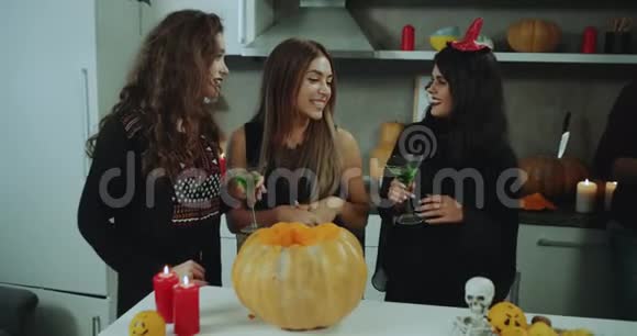 在万圣节派对上女孩们在厨房里聊天开心地微笑着看着一个大南瓜里面有非常棒的南瓜视频的预览图