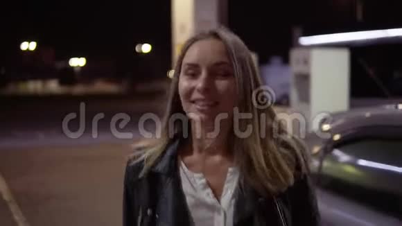 浪漫的微笑的女人在加州的加油站汽车在后台行走和摆姿势前景夜间视频的预览图