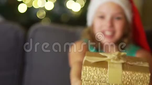 戴着圣诞帽的少女给了一个带丝带的金盒子圣诞礼物亲密肖像除夕视频的预览图