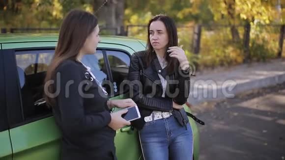 两个漂亮的女人在绿车旁说话视频的预览图