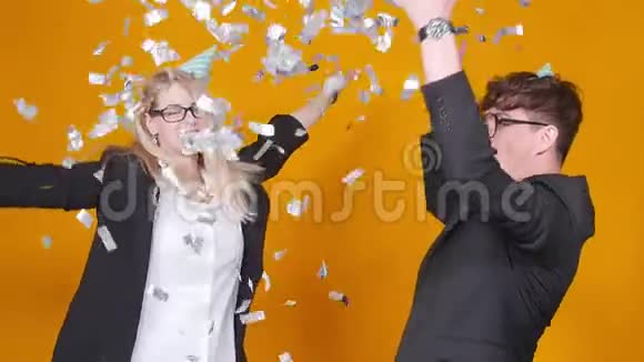节日和生日的概念年轻的幸福夫妇戴着橙色背景的帽子和五彩纸屑跳舞视频的预览图