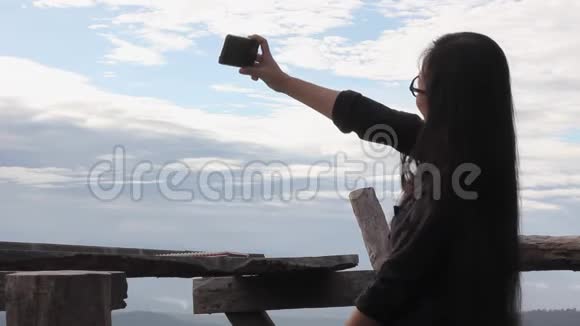 女人用智能手机或手机在蓝天和云彩的背景下拍摄照片或自拍视频的预览图