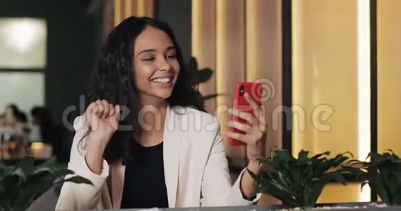 漂亮的年轻商务女性坐在现代办公室或咖啡馆里通过智能手机上的视频聊天交谈她笑了视频的预览图