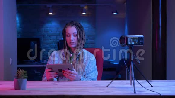 年轻的女性博客写手戴着可怕的耳机用平板电脑现场直播并显示绿色视频的预览图