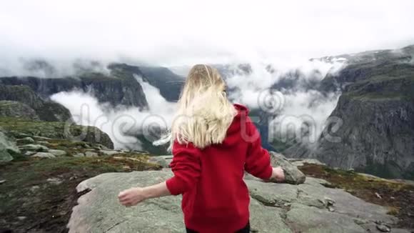 一个留着长发穿着红色运动衫的年轻女孩走在山里挪威峡湾视频的预览图