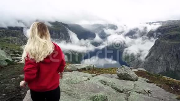 一个留着长发穿着红色运动衫的年轻女孩走在山里挪威峡湾视频的预览图