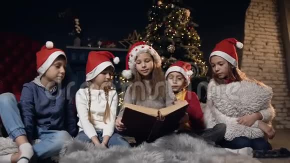 时尚可爱的孩子们一边看书一边在圣诞树附近的房间里放松视频的预览图