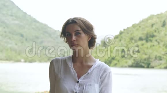肖像少女夏日江畔与青山山水面对湖岸上的年轻女子山峦叠翠视频的预览图