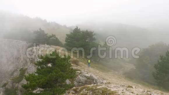 一个背着背包的年轻人走在布满云的岩石山脉上视频的预览图