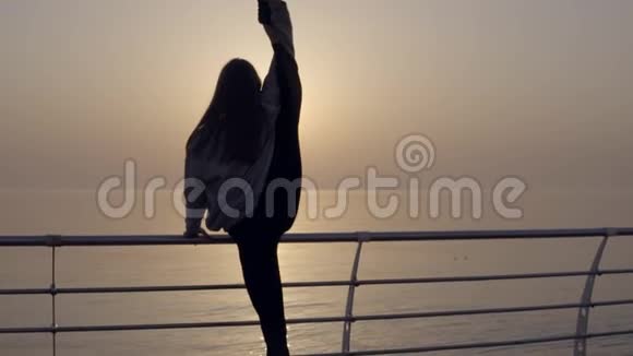 苗条的女人长腿在海边日出时做伸展运动完美的身体她的腿在头上视频的预览图
