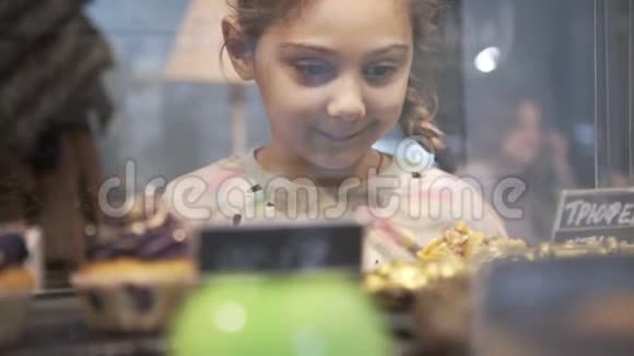 小女孩选择了蛋糕和甜点展示各种蛋糕的蛋糕店橱窗视频的预览图