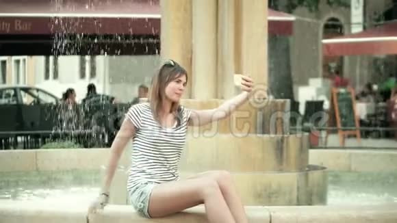 美丽的年轻女子用手机在喷泉附近自拍视频的预览图