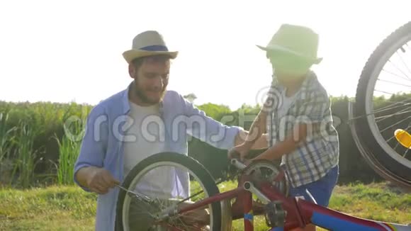 农村的家庭周末孩子和爸爸在大自然的背景下用背光修理自行车视频的预览图