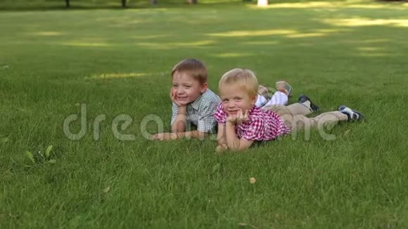 两个穿着衬衫的可爱小男孩躺在绿草上微笑着肖像视频的预览图