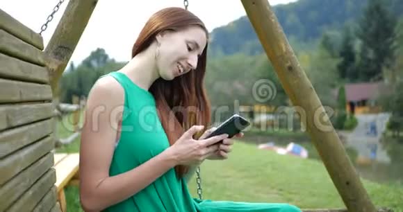 4K女孩坐在秋千凳上在山上用她的手机视频的预览图