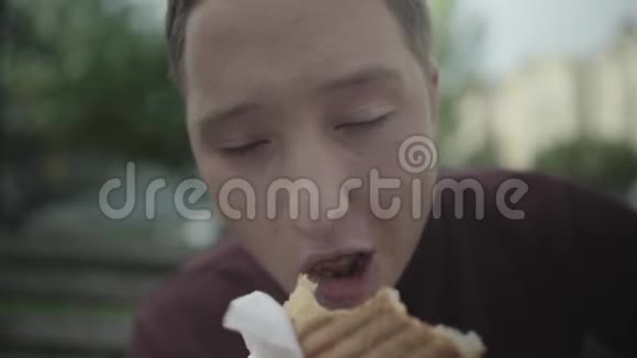 年轻人在户外吃三明治把脸贴紧视频的预览图