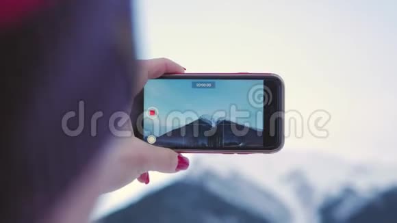 年轻的女人用她的智能手机在山上拍摄冬天的大自然视频的预览图