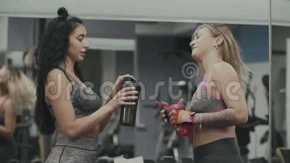 两个有魅力的女孩在健身房里喝蛋白奶昔饮料视频的预览图