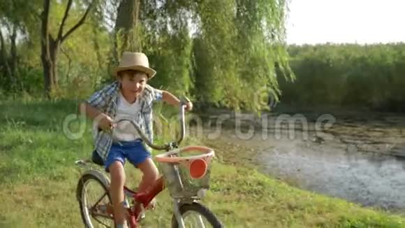 小男孩在湖和大自然的背景下在乡下骑自行车玩得很开心视频的预览图