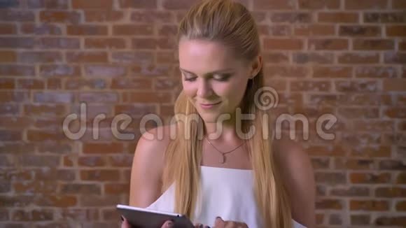 年轻可爱的白人金发女人用平板电脑刷卡显示绿色屏幕背景是砖墙视频的预览图
