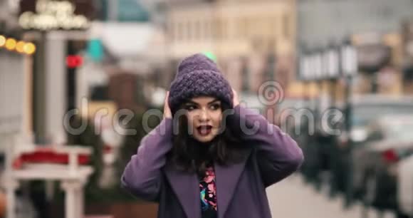 穿着紫色冬帽和外套的迷人女孩用鲜艳的化妆在街上行走视频的预览图