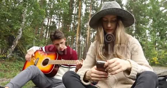 年轻的男人和女人拿着吉他坐在森林里视频的预览图